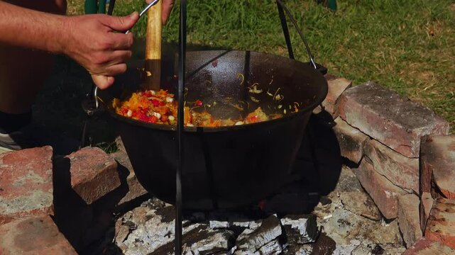 A traditional Romanian cooking moment where tomato puree is poured into a cauldron over a wood fire. This rustic outdoor scene captures the making of authentic zacusca, a flavorful spread