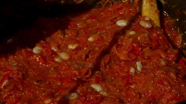 A traditional Romanian cooking moment where tomato puree is poured into a cauldron over a wood fire. This rustic outdoor scene captures the making of authentic zacusca, a flavorful spread