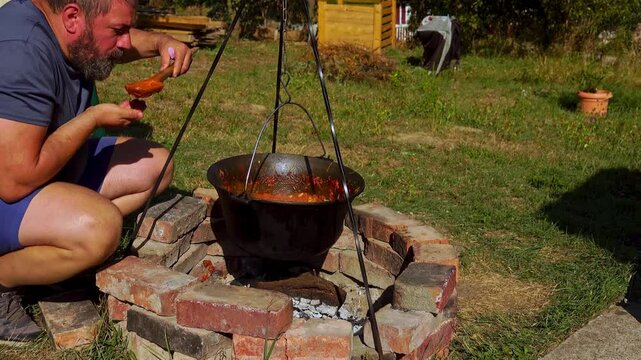 A traditional Romanian cooking moment where tomato puree is poured into a cauldron over a wood fire. This rustic outdoor scene captures the making of authentic zacusca, a flavorful spread.