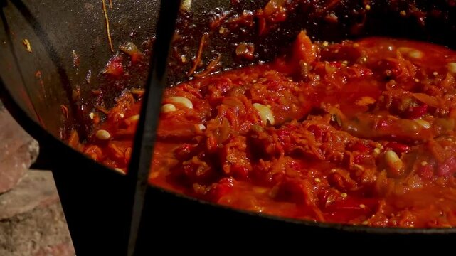 A traditional Romanian cooking moment where tomato puree is poured into a cauldron over a wood fire. This rustic outdoor scene captures the making of authentic zacusca, a flavorful spread