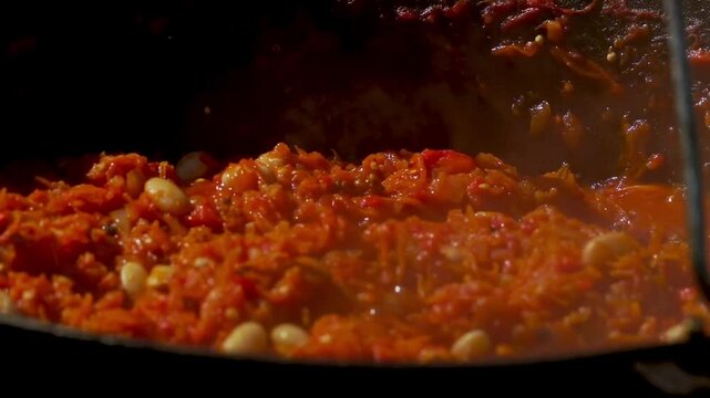 A traditional Romanian cooking moment where tomato puree is poured into a cauldron over a wood fire. This rustic outdoor scene captures the making of authentic zacusca, a flavorful spread