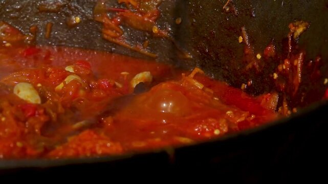 A traditional Romanian cooking moment where tomato puree is poured into a cauldron over a wood fire. This rustic outdoor scene captures the making of authentic zacusca, a flavorful spread