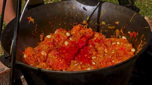 A traditional Romanian cooking moment where tomato puree is poured into a cauldron over a wood fire. This rustic outdoor scene captures the making of authentic zacusca, a flavorful spread