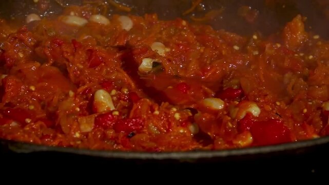 A traditional Romanian cooking moment where tomato puree is poured into a cauldron over a wood fire. This rustic outdoor scene captures the making of authentic zacusca, a flavorful spread