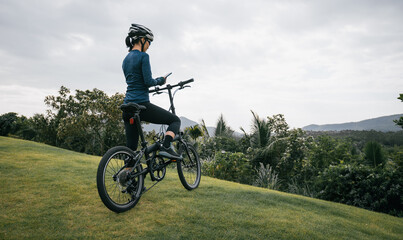 Fototapeta premium Woman cyclist using a smartphone on tropical mountain peak
