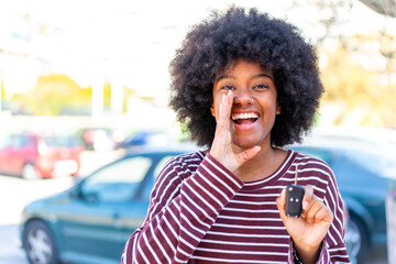 African American girl holding car keys at outdoors shouting with mouth wide open
