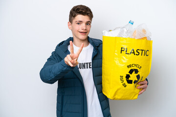 Teenager Russian holding a bag full of plastic bottles to recycle on white background smiling and...