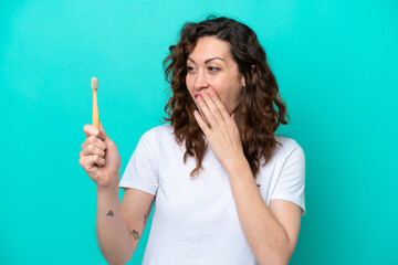 Young caucasian woman brushing teeth isolated on blue background with surprise and shocked facial...