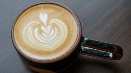 Cup of hot cappuccino with latte art on wooden table. Image in top view