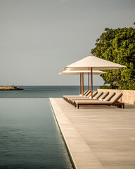 A tranquil poolside view with loungers and umbrellas overlooking the serene ocean at sunset