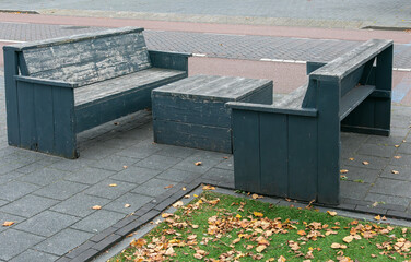 two wooden benches and wooden table are outside on the sidewalk