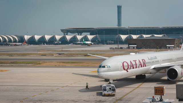 April 5, 2024 - Bankok, Thailand - A large white Qatar airline airplane is push back by airport tow tug to apron jet bridge for boarding passenger at Suvarnabhumi Airport terminal.