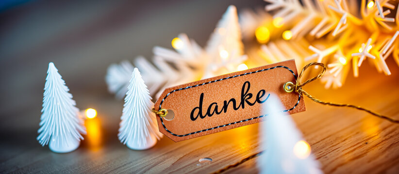 brown tag with the word danke lies on a wooden surface decorated with white trees lights.