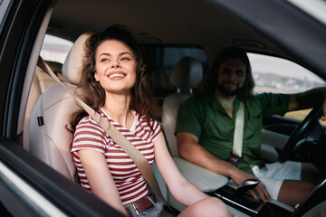 Smiling young woman in a car with a male companion, enjoying the view on a sunny day