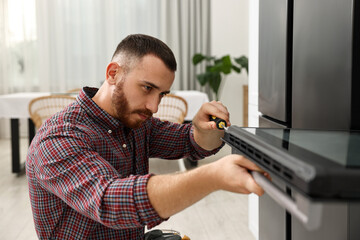 Repairman with screwdriver fixing oven at home