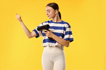 Fototapeta premium Woman using percussive massager to relieve bicep on yellow background