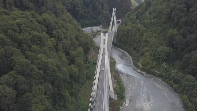 Aerial around epic modern cable-stayed bridge Adler road Krasnaya polyana Sochi Russia suburban freeway cars traffic among high mountains. Natural landscape green slopes. Travel landmark.