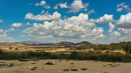 Spanish countryside with mountains and vegetation under blue cloudy sky.