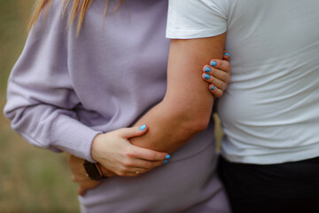 A pregnant woman in the arms of her husband. Summer sunny weather. A couple in love are hugging.