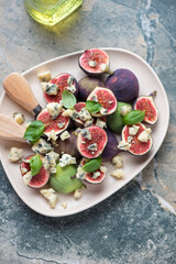 Plate with fresh fig fruits and blue cheese, vertical shot on a grey and beige granite background, high angle view