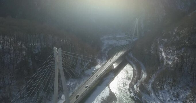 Aerial around epic modern cable-stayed bridge Adler road Krasnaya polyana Sochi Russia suburban freeway cars traffic among high mountains. Natural landscape green slopes. Travel landmark.