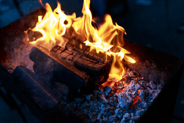 Obraz premium Burning wood for cooking on the grill. Tongues of flame, smoke, coal and ash. Burning hot charcoal. The tongues of flame and ashes. Forge horn, brazier. 