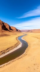 Fototapeta premium Winding river through a vast desert landscape under a clear blue sky.