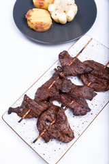 White tray with a portion of Anticuchos, a traditional Peruvian dish accompanied with potatoes and corn.