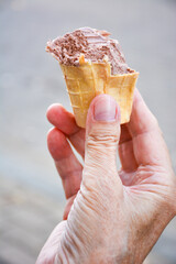 Ice cream cone in a hand. Male hand holding wafer cone with a half-eaten chocolate ice cream on a blurred background