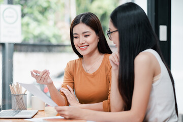 Two young women discussing documents in a modern office, showcasing teamwork and collaboration.