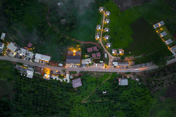 Aerial shot of a village at dusk, showcasing illuminated streets, houses, and lush green surroundings. © Satori Studio