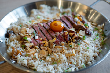 Beef with garlic fried rice, a dish of rice topped with rare beef served with pickled egg yolk with fish sauce on a pan
