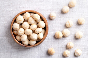Macadamia nuts, roasted and salted, in a wooden bowl on linen fabric. Also known as Queensland nut, bush nut, maroochi nut, bauple and Hawaii nuts. Ready-to-eat snack nuts. Close-up, from above. Photo