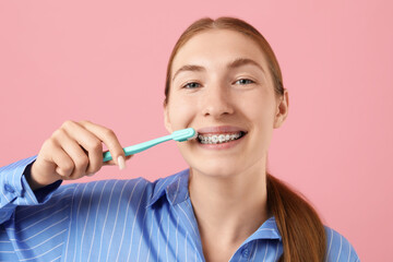 Girl with braces cleaning teeth on pink background