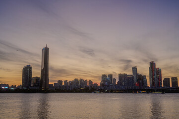 Obraz premium Sunset and silhouette view of 63 Building and high rise buildings of financial district with Wonhyo Bridge on Han River at Yeouido near Yeongdeungpo-gu, Seoul, South Korea