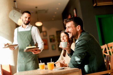 Waiter serves delicious vegetarian dishes to cheerful diners in a vibrant café during a sunny afternoon