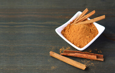 Ground cinnamon powder with cinnamon sticks on black wooden background