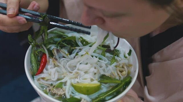 Caucasian woman eats traditional vietnamese beef noodle soup pho bo.