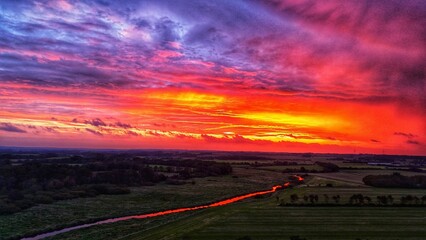 Vibrant sunset over rural landscape with river reflection.