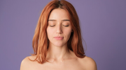 Close-up of red-haired woman with closed eyes in studio on purple background. Beautiful girl poses in studio with blank space on violet wall for your promotion