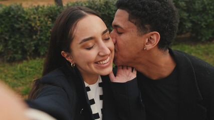 Multiracial couple taking selfie with smartphone in park