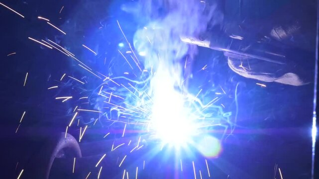 The welder is welding to structural steel with shielding metal arc welding process (manual electrode welding). close-up welder works with electrode in protective helmet and glows
