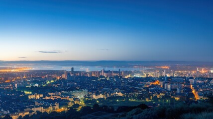 Fototapeta premium Panoramic city skyline at dusk with lights and distant mountains.