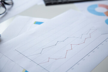 Lots of charts, keyboard, glasses on the desktop. Top view, flat lay