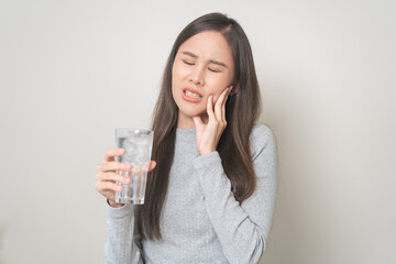 Suffering from toothache, hurt asian young woman touch cheek, face expression ache or feel pain, sensitive molar teeth, hand holding glass of water with ice, inflammation when drink cold, healthcare.