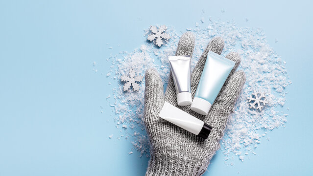 Winter skincare concept with a hand in grey mitten holding a winter cosmetic set.