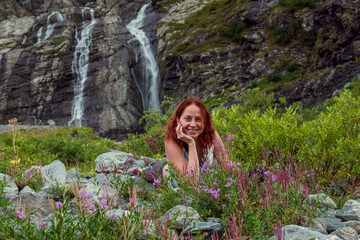 Happy woman enjoying her free time while lying on grass in the mountains, waterfalls background