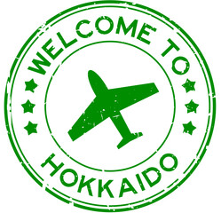 Grunge green welcome to hokkaido with airplane icon round rubber seal stamp on white background