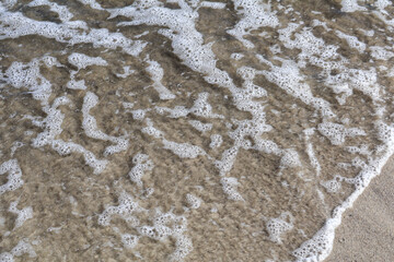 Foamy Ocean Waves Gently Reaching Sandy Beach Shoreline Close-Up