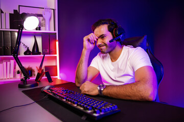 Serious face gaming streamer concentrating gaming players trying to pass at mission completed, using headset and mic for communicate others on streaming live at neon lighting studio room. Surmise.
